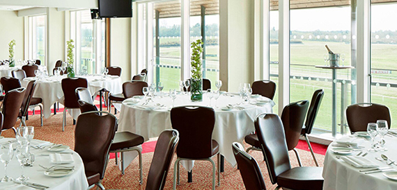 Dining room with round white-clothed tables overlooking the racecourse
