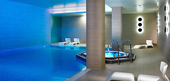 Indoor spa pool with a jacuzzi and white loungers under blue lighting