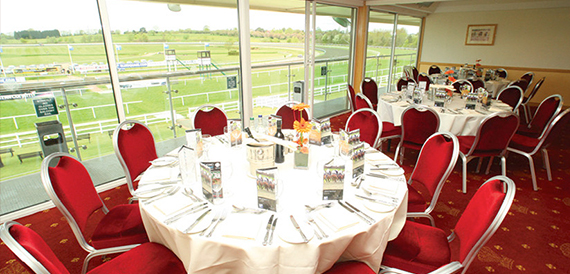 Dining room with round tables and red chairs overlooking the racecourse