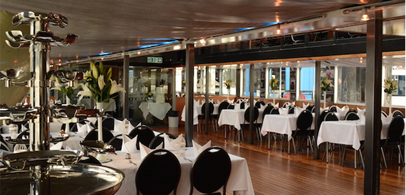 Dining tables set with white linen and lily centrepieces along the boat's deck.