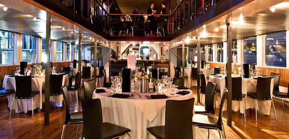 Round dining tables set with white linen beneath a mezzanine level at night.