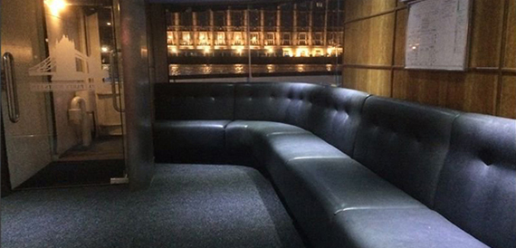 Black leather bench seating on the boat deck at night with river lights outside.