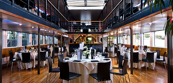 Two-tier boat interior set with round tables, white linen and black chairs.