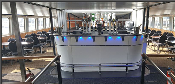 Onboard bar with beer taps and blue lighting, dining tables either side.