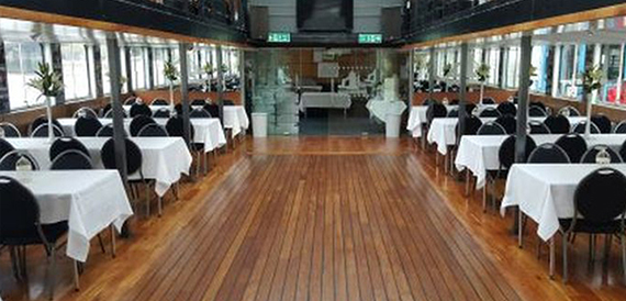 Rows of dining tables with white linen and black chairs along a wooden deck.