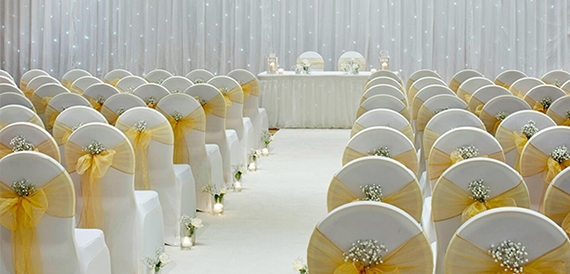 Wedding ceremony aisle lined with white chair covers and gold organza sashes