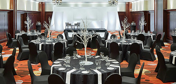 Ballroom set for a banquet with round tables, black chair covers and white branch centrepieces