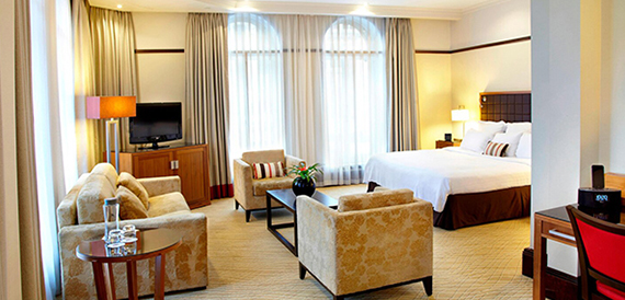 Hotel suite with a bed, cream armchairs and a coffee table