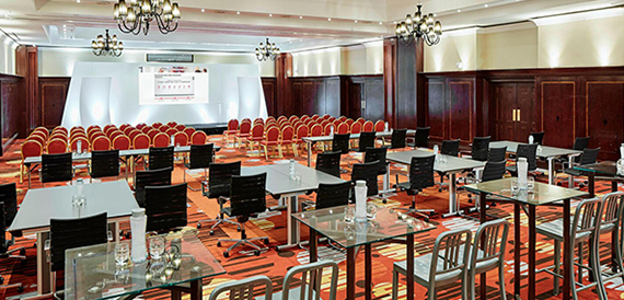 Large conference room set theatre-style with red chairs facing a stage and screen