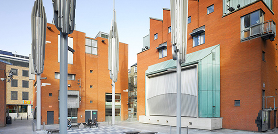 Exterior of the brick buildings with folded canopy sails overhead in daylight.