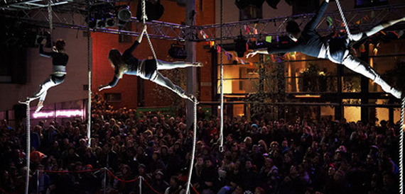 Aerial acrobat performing above a crowd at an outdoor circus event.
