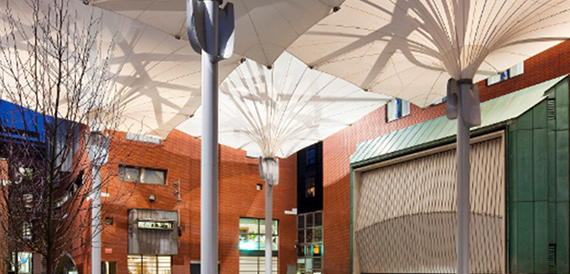 Daytime view of the tensile fabric canopy above brick buildings, courtyard empty.