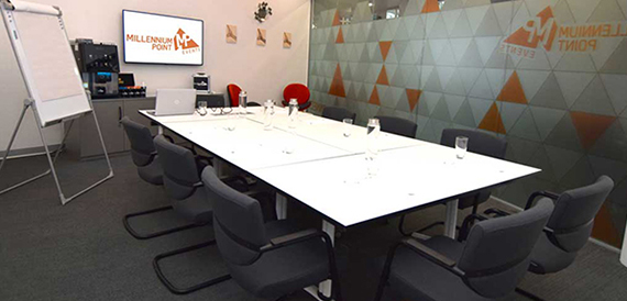 Boardroom with a white table, grey chairs and a wall-mounted screen.
