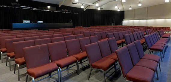 Auditorium with rows of red seating facing a curtained stage.