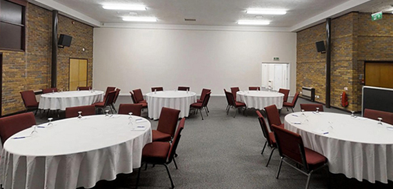 Meeting room set cabaret-style with round tables and red chairs against a brick wall.
