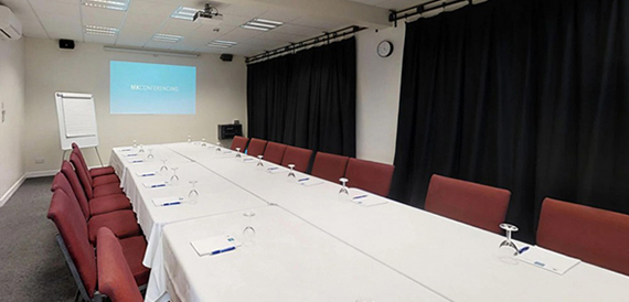 Boardroom with a long table, red chairs and a projector screen.