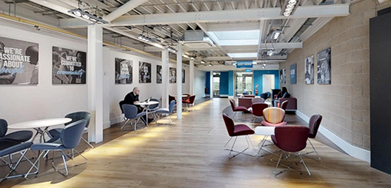Breakout corridor with round tables, blue and burgundy chairs and framed wall art.