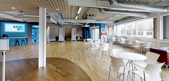 Breakout space with white round tables, chairs and an exposed ductwork ceiling.