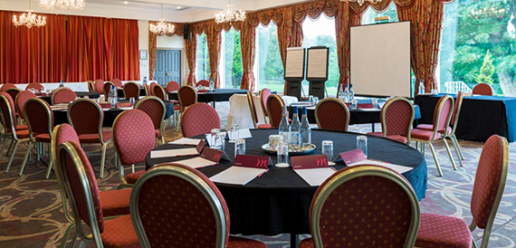 Meeting room set up boardroom-style with red chairs, chandeliers and long curtains.