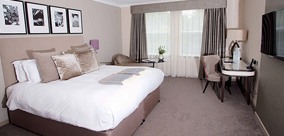 Hotel bedroom with a double bed, framed prints above the headboard and a desk.
