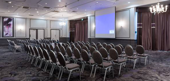 Conference room with theatre-style seating facing a projector screen and chandelier.