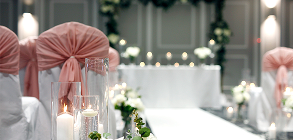 Table setting with pink drapery, lit candles and glass vases in soft focus.