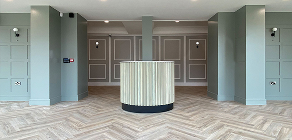 Reception area with a curved cream desk and herringbone wood flooring.