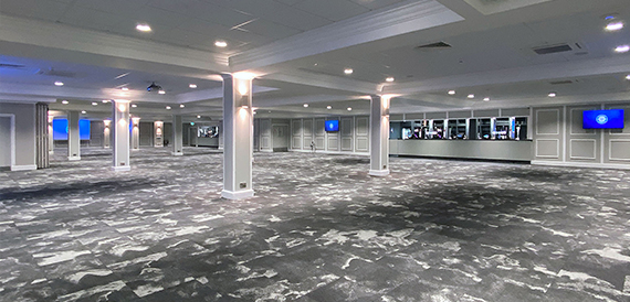 Large empty function hall with grey patterned carpet and white pillars.