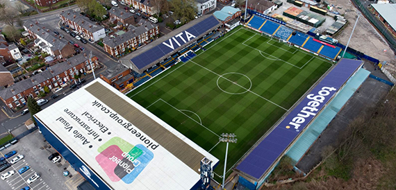Aerial view of a football stadium pitch surrounded by stands and terraced housing.