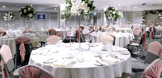 Wedding reception table dressed in white linen with pink chair covers and tall floral displays.