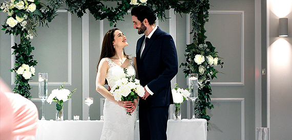 Bride and groom embracing and smiling together in front of greenery.