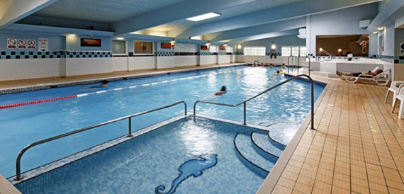 Indoor swimming pool with sun loungers and a seahorse mosaic on the floor.