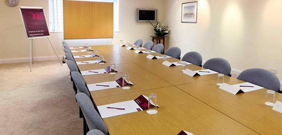 Boardroom with a long table, grey chairs and conference folders set out.