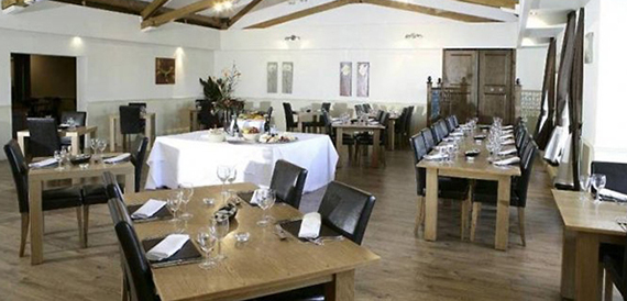 Dining room with wooden tables, black leather chairs and exposed roof beams.