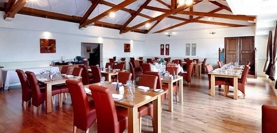 Restaurant with exposed wooden roof beams, red leather chairs and wooden tables.