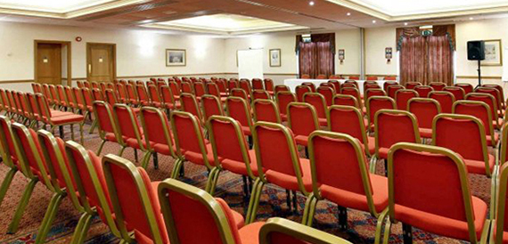 Conference room set theatre-style with rows of red chairs and framed pictures on the wall.