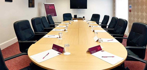 Boardroom with an oval table, black leather chairs and a wall-mounted screen.
