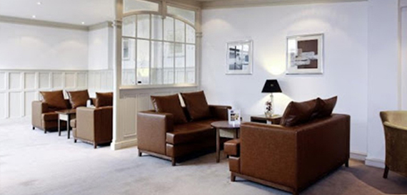 Lounge area with brown leather sofas, armchairs and a large arched window.