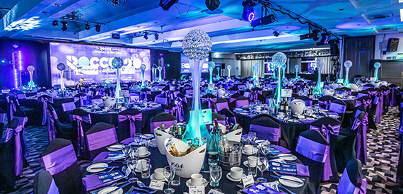 Awards dinner tables under blue lighting with a large video screen.