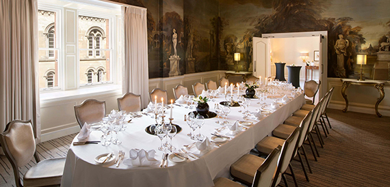 Long dining table set formally beneath painted mural walls
