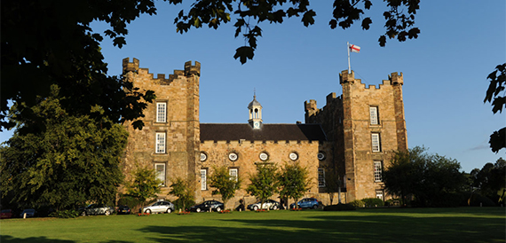 Exterior of Lumley Castle with its stone towers set against lawns and a clear sky