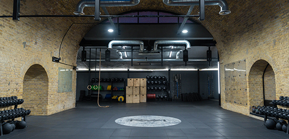 Gym floor with pull-up rig, weights and storage boxes under a brick archway