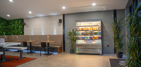 Cafe area with a drinks fridge, bench seating and wooden tables