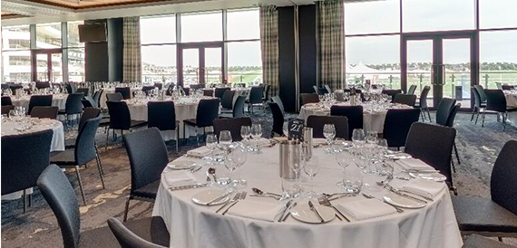 Dining room with round tables set with glassware beside large windows