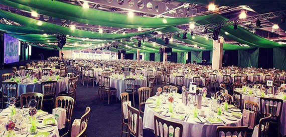 Banqueting hall with green drapery and round tables set for dinner