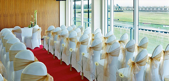 Wedding ceremony aisle lined with chair covers and gold sashes overlooking the racecourse