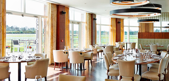 Restaurant dining area with round tables, cream chairs and views over open fields