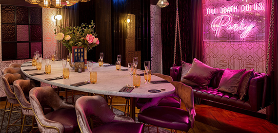 Private dining table with pink velvet chairs beneath a neon party sign