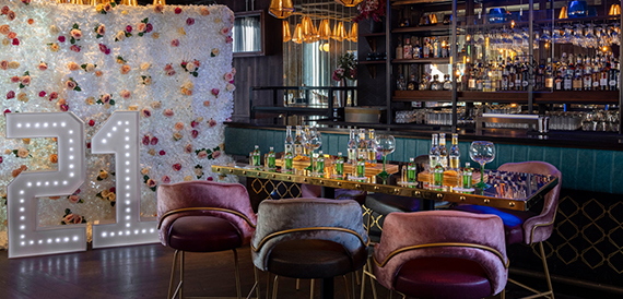 Bar area with a flower wall, light-up number decoration and velvet chairs beside the counter