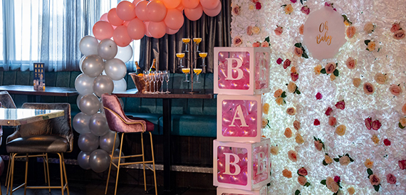 Baby shower decor with a balloon arch, light-up letter blocks and a flower wall